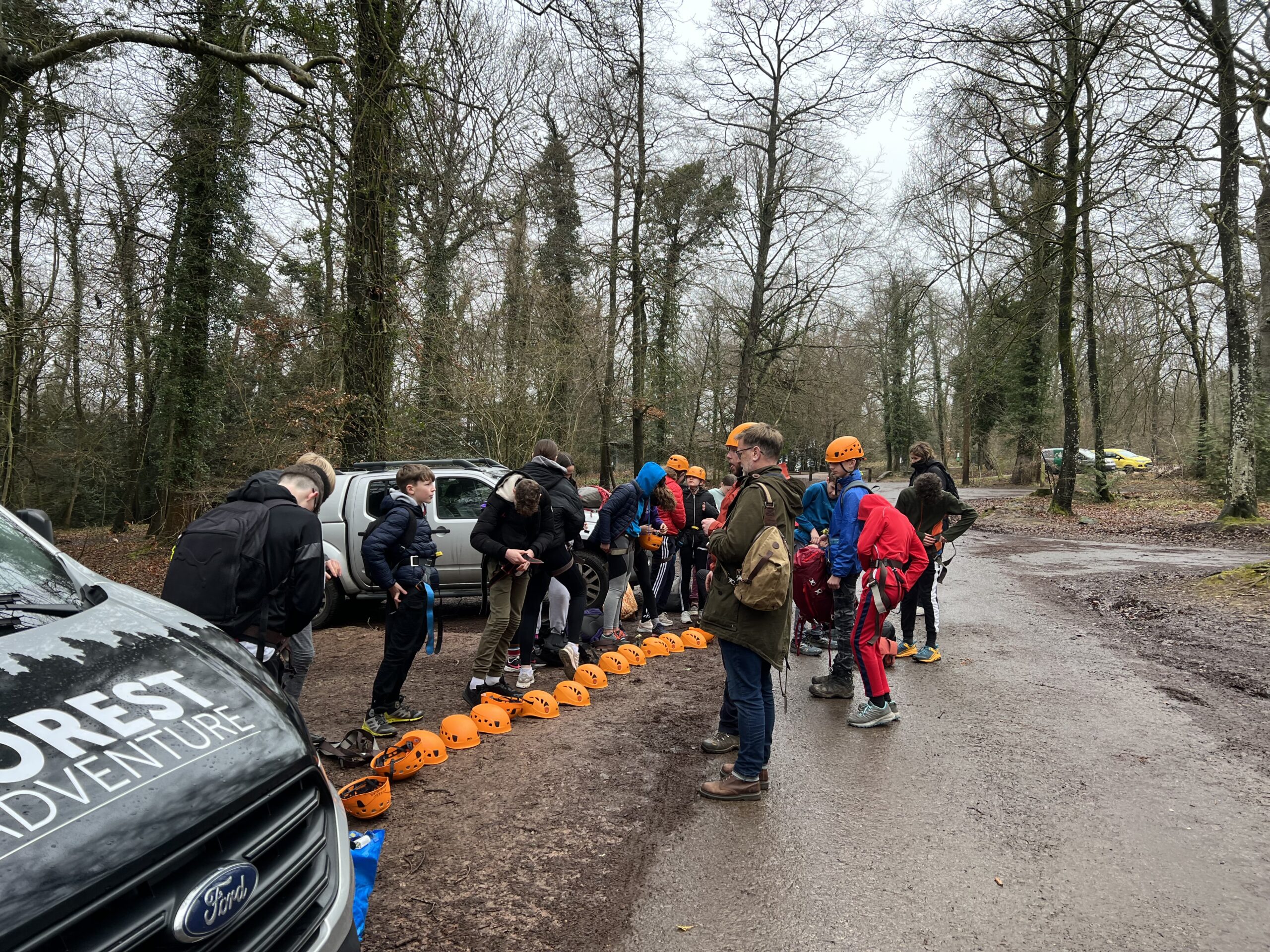 A group of children getting into climbing harnesses and helmets in a car park.