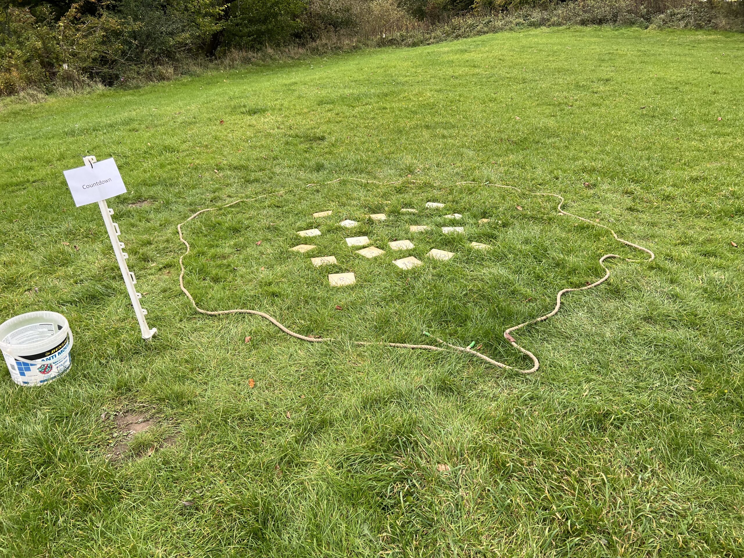 Tiles laid out within a ring of rope next to a sign in a filed.