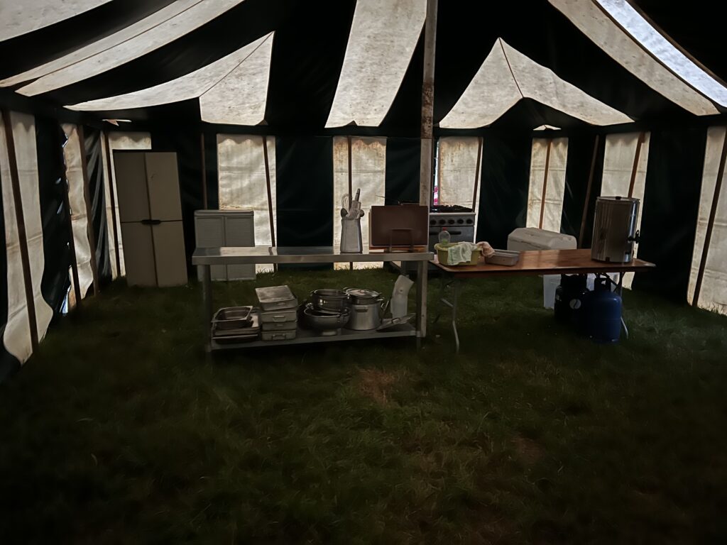 A photo of the inside of a stripy marquee containing a cooker and two tables with cooking equipment atop them.