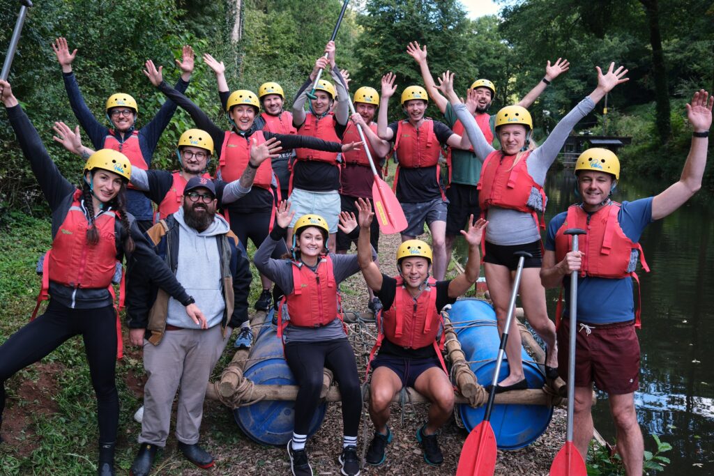 Group of people with helmets and life jackets on top of a raft waving